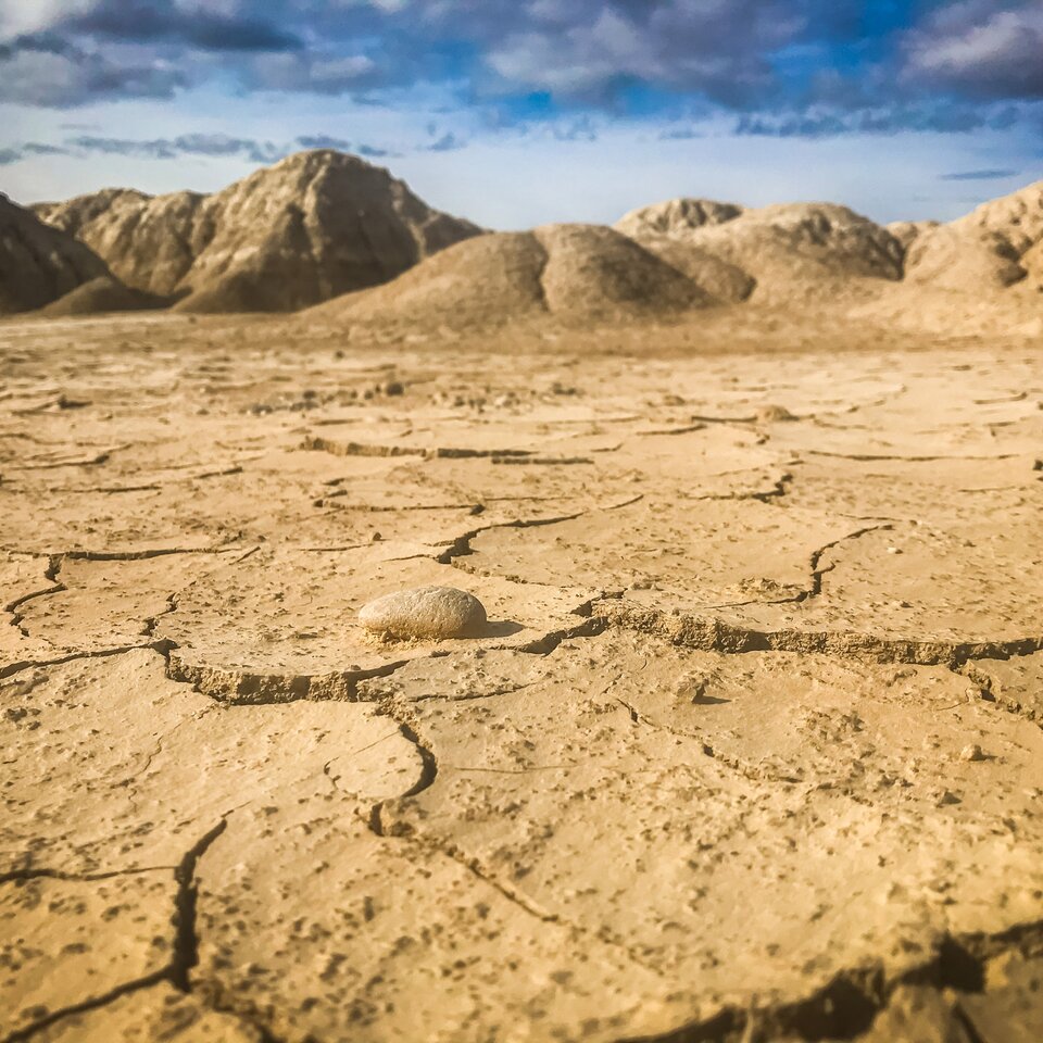 Bild vom Reisebericht über einen Trip in die Pyrenäen mit dem Wohnmobil zeigt sandig-trockenen Boden mit Rissen, im Hintergrund sind Hügel zu sehen. 