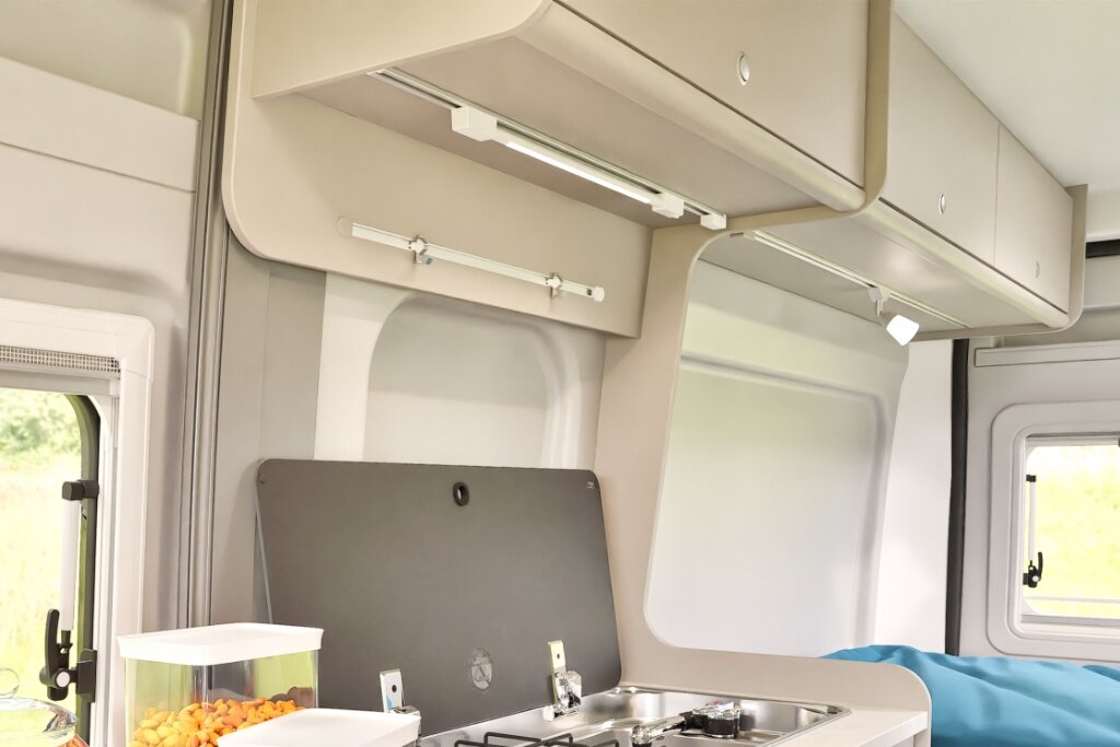 Carado motorhome interior with kitchenette, overhead cabinets and a window beside the bed