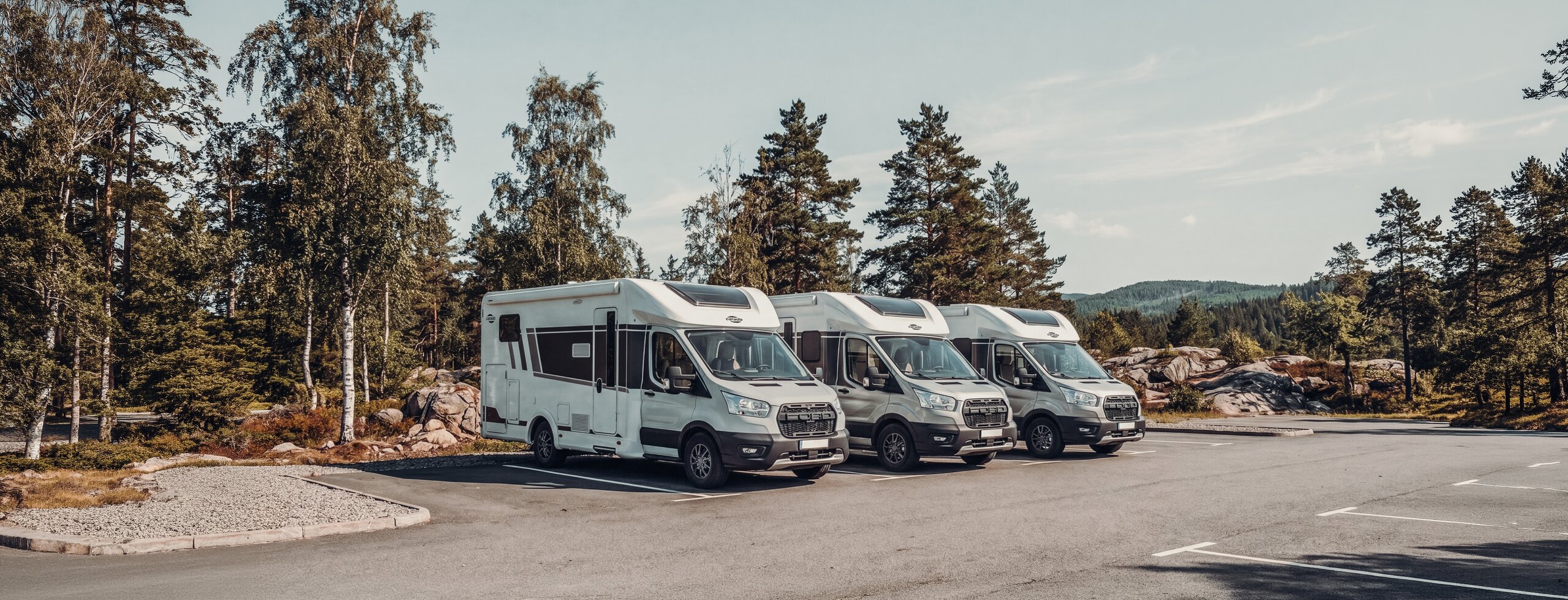 Three Carado motorhomes parked at the edge of a forest, shown from the front and the side
