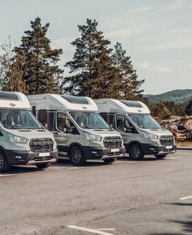 Three Carado motorhomes parked side by side in a side view, framed by trees
