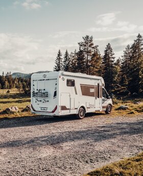 Carado T 338 semi-integrated motorhome on a gravel path at the edge of the forest, rear and side view