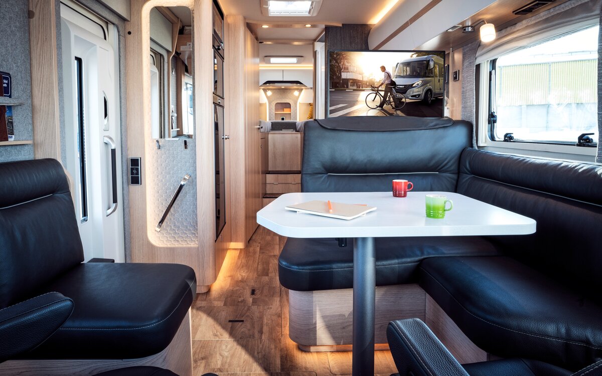 Zitgroep in zwart lederlook met gedekte tafel en zicht op tv-plasma en achtergedeelte in de HYMER B MasterLine