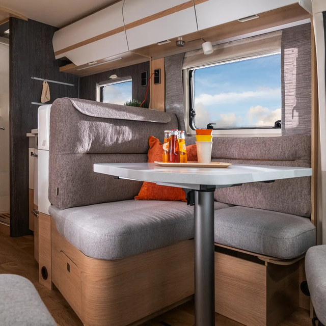 Uitzicht vanuit de overdekte zithoek en het keukenblok door de ramen van de HYMER B ML-T 780 op de zonnige blauwe lucht