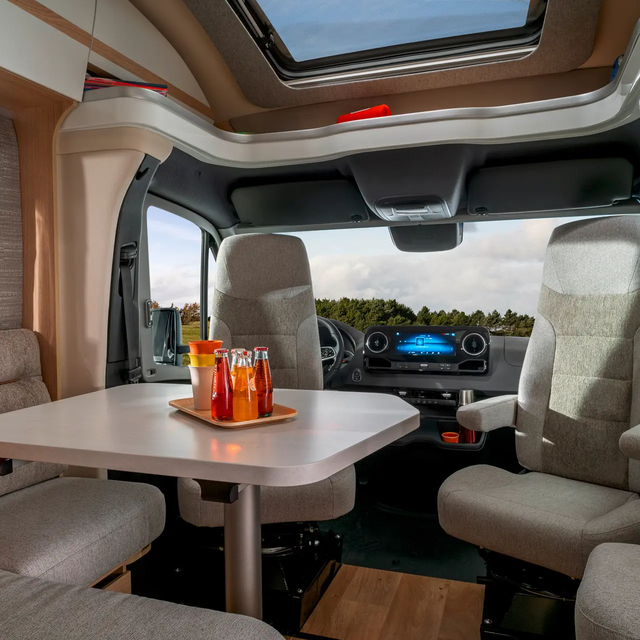 Uitzicht vanuit de zitgroep met bestuurdersstoelen en navicockpit in de middenconsole door het raam van de HYMER B-ML T naar de lucht en het bos