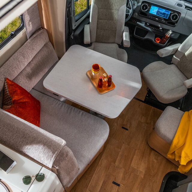 Zitgroep met bestuurdersstoelen en rode kussens en een mobiele telefoon en zonnebril op de plank naar de keuken in de HYMER B ML-T 780