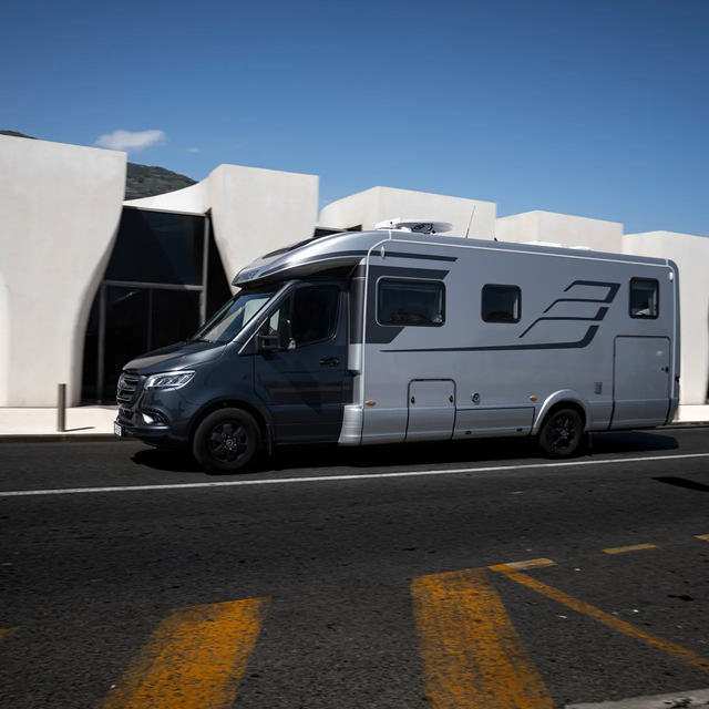 HYMER B MasterLine T voor een modern wit gebouw met grote glazen gevels, blauwe lucht en palmbomen
