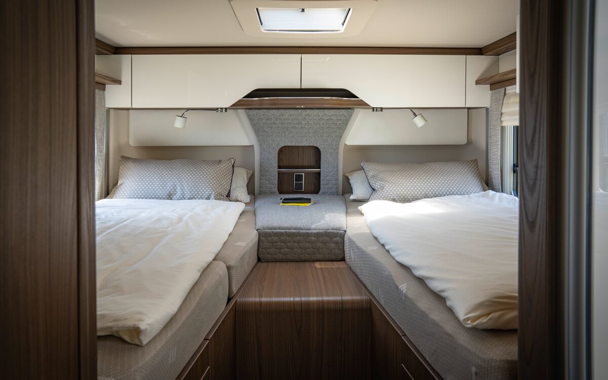 Slaapgedeelte in de camper met twee eenpersoonsbedden in de lengterichting, een middenconsole ertussen voor opslag en keukengerei en boven het hoofdeind afgesloten opbergvakken.