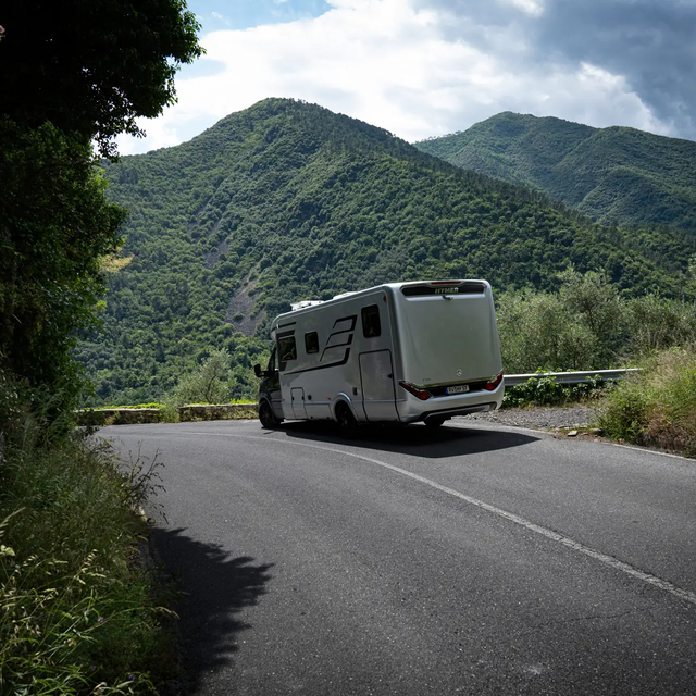 HYMER B-klasse MasterLine T camper bergafwaarts rijdend in een groen bergpanorama met blauwe lucht