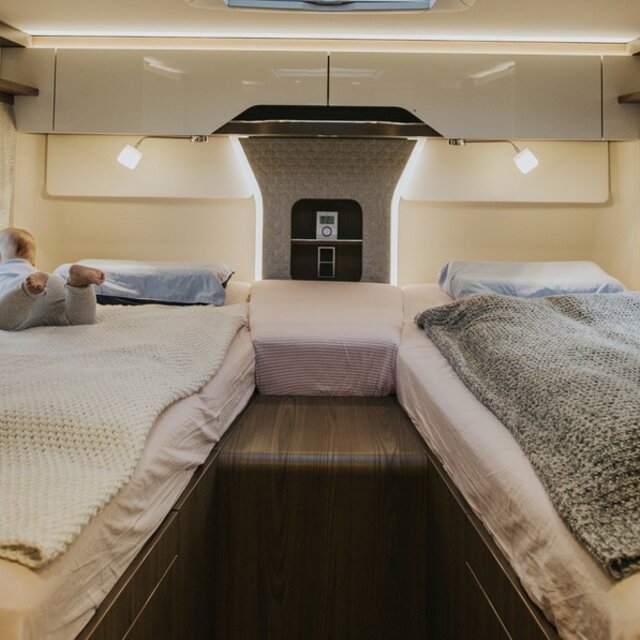 Kleuter op het linker eenpersoonsbed in de lengterichting achterin de camper; gezellige woonsfeer dankzij aangename sfeerverlichting.