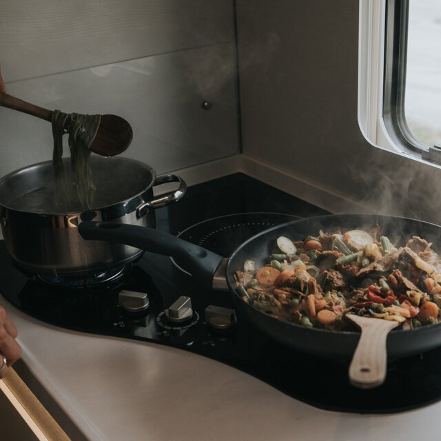 Het bereiden van voedsel (pasta in een pan en groenten in een pan) op een hybride kooktoestel in een camper