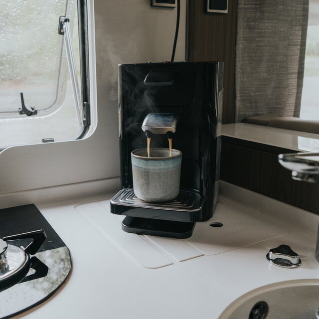 Koffiezetapparaat op het aanrecht in een camper, de vers gezette koffie loopt in een grijs aardewerken kopje 