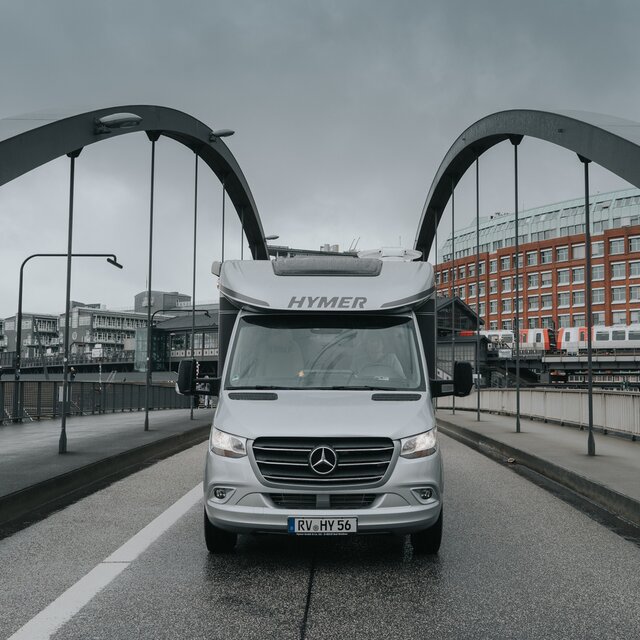 Vooraanzicht van een halfintegraal HYMER-camper op een stadsbrug bij bewolkt weer