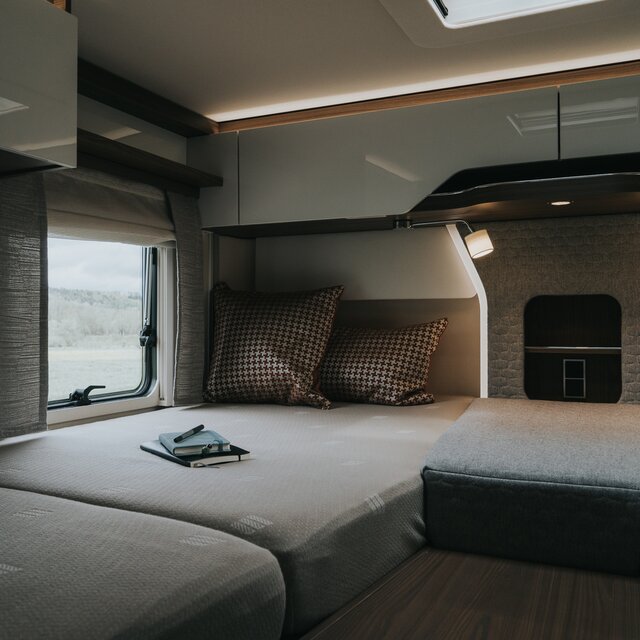 Slaapgedeelte met decoratieve kussens op het bed in de camper achterin met ingeschakelde leeslampen en sfeerverlichting