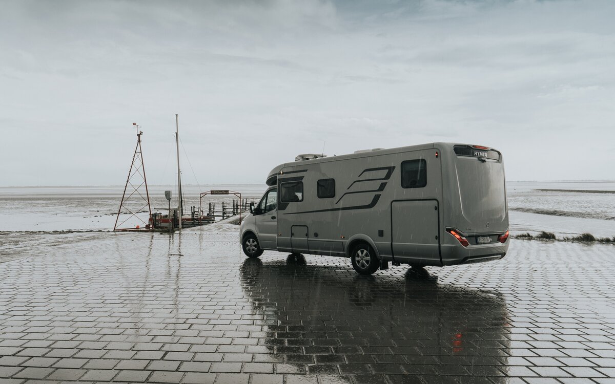 Halfintegraal HYMER camper (achter/zijaanzicht) staat bij regenachtig weer op verhard terrein aan zee