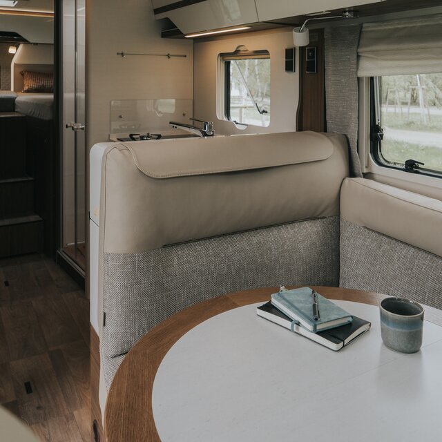Woonruimte in een camper met lichte L-vormige zitgroep en ronde tafel met echt houten frame