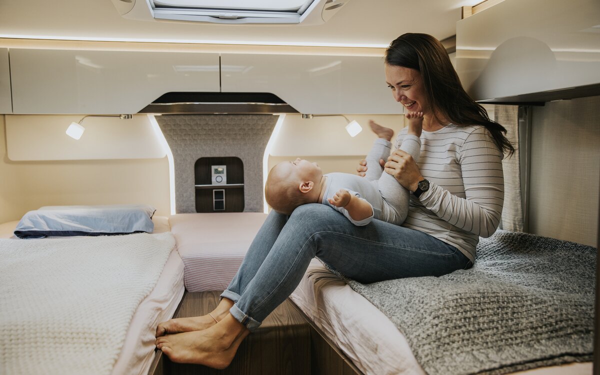 Jonge vrouw zittend op een bed achteraan in een camper met een baby op haar schoot