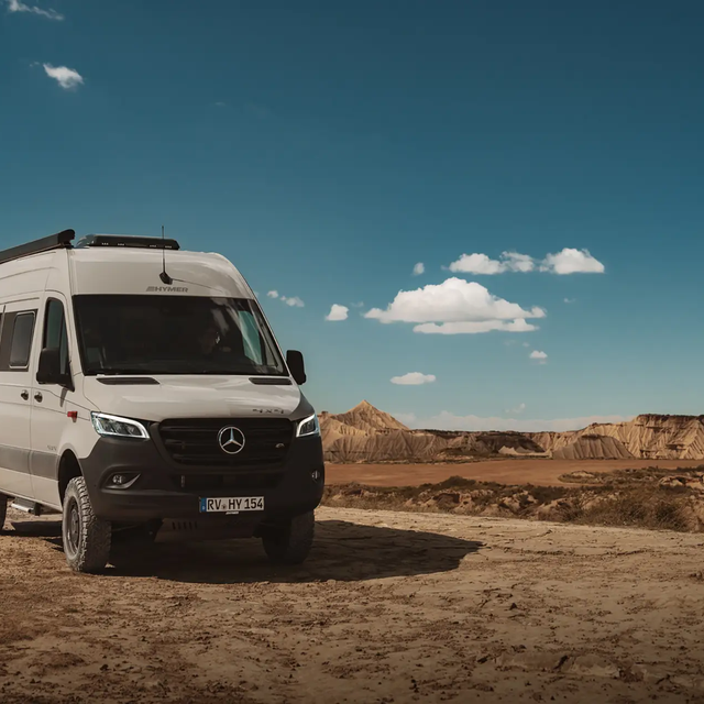Light grey campervan from HYMER is slightly angled with front facing forward in a barren, desert-like landscape under a blue sky with few white clouds