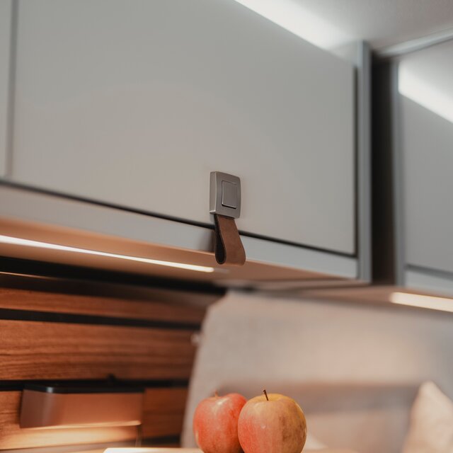 Light overhead cabinet with brown leather strap, two apples are visible at the bottom edge of the picture