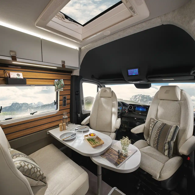 The living area of the HYMER Grand Canyon S in the Ivy Green style world is visible from the kitchen. Behind it, the driver's cab is visible.