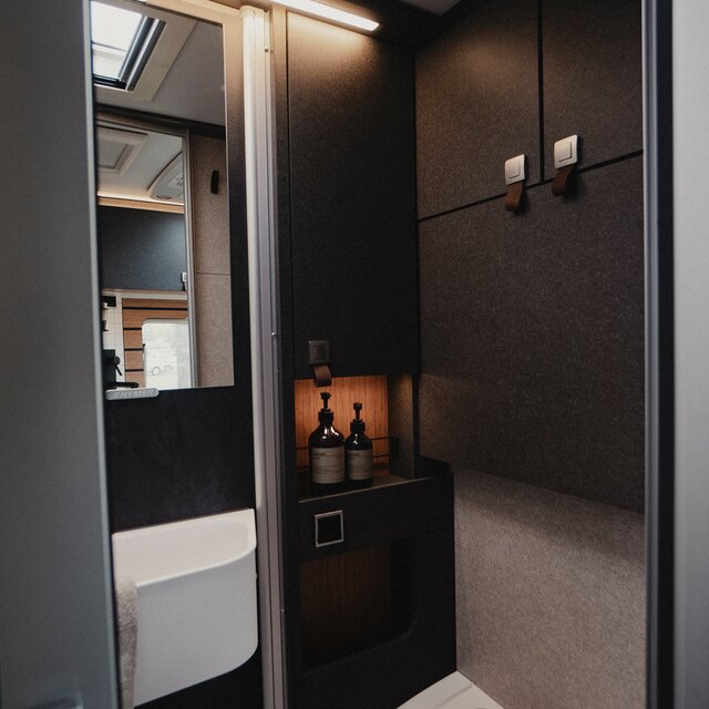 Bathroom in a motorhome, shower cubicle with sink, mirror, cassette toilet, storage and cabinet units in black