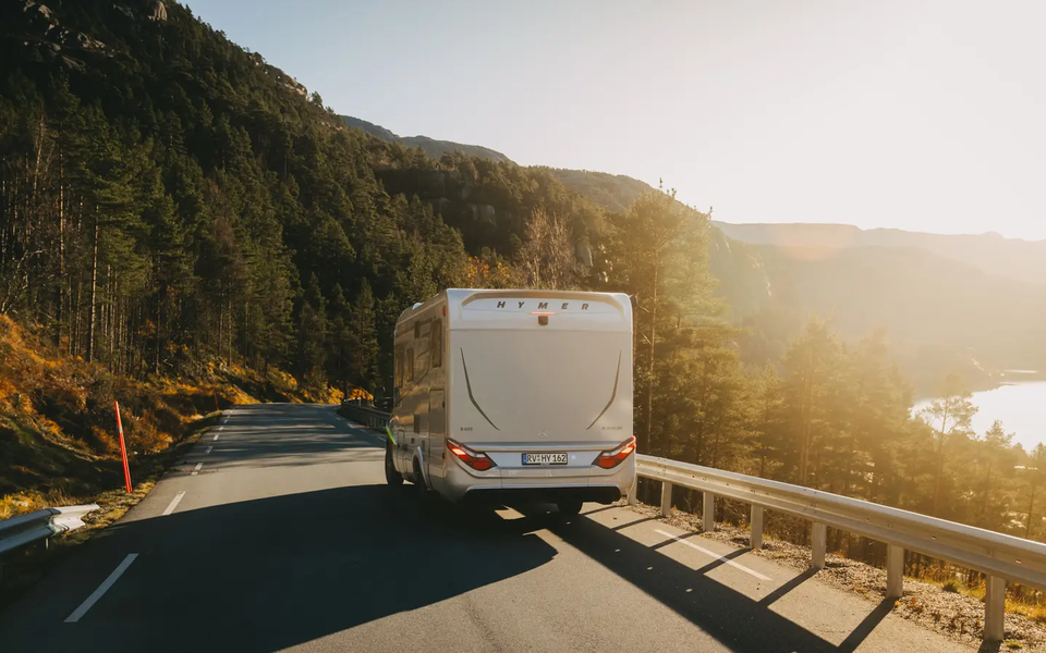 Rear view of the HYMER B-MC T BlackLine, vehicle driving on a country road, forest on the left background, lake on the right background
