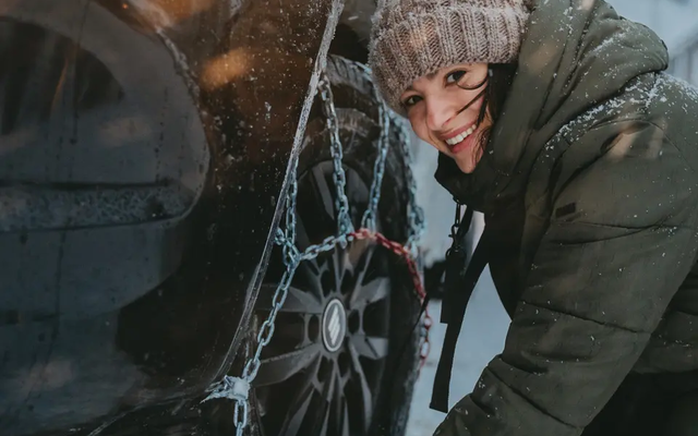 View of a woman, she is putting snow chains on a tire