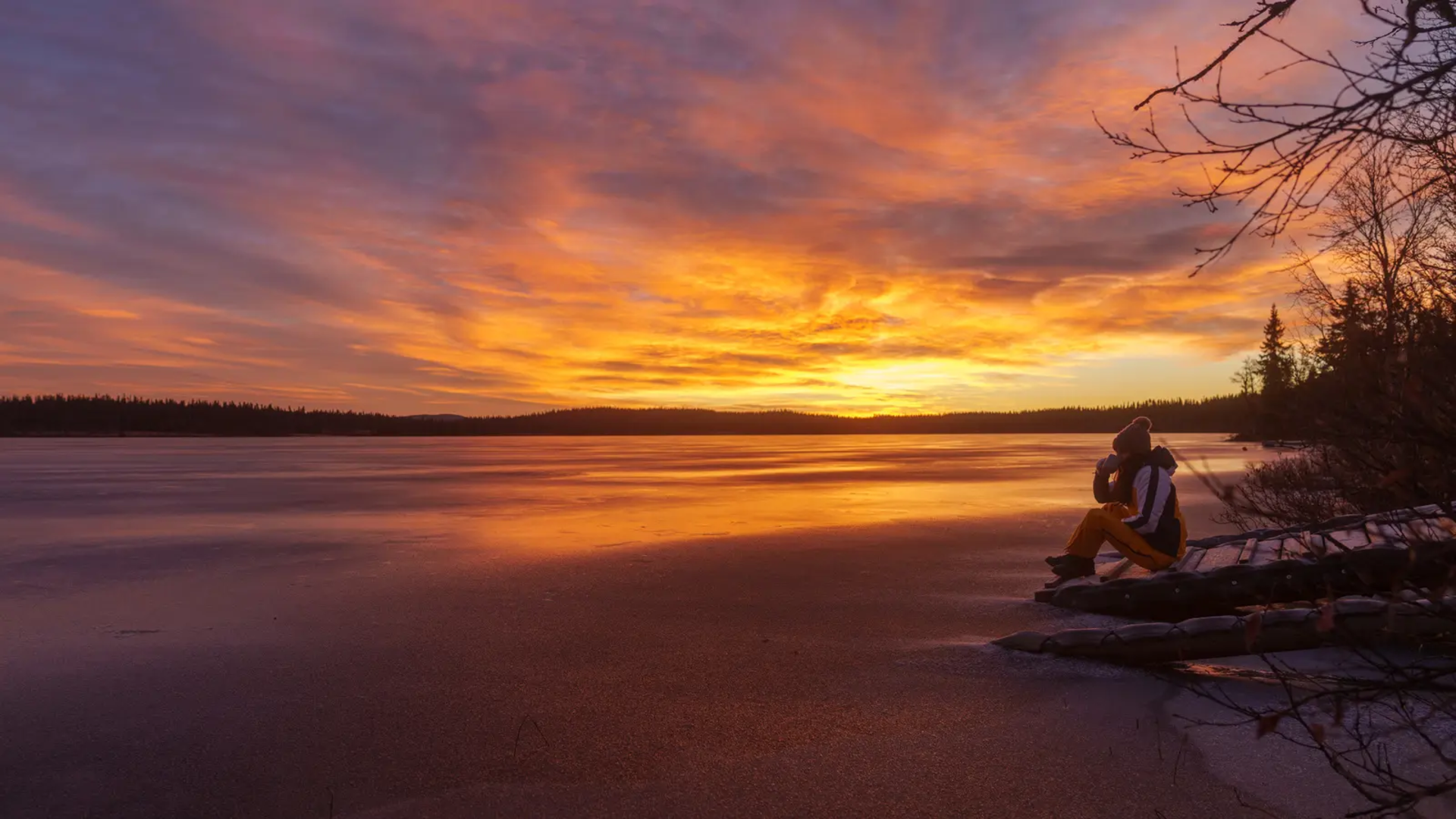 View of a lake with beautiful sunset, a woman sitting on a jetty in the right foreground